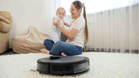 Robot vacuum cleaner helping woman doing chores while she spend time with baby son. Concept of hygiene, household gadgets and robots at modern life.の写真素材