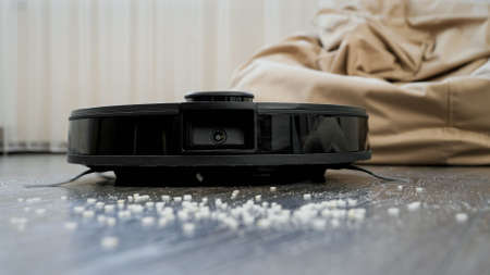 Closeup of robot vacuum cleaner removing dust and crumbs on floor at living room. Concept of hygiene, household gadgets and robots at modern life.の写真素材