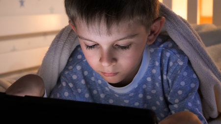 Little boy lying in bed with tablet computer and watching video. Children education, development,...