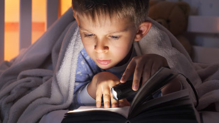Closeup of boy holding flashlight reading book in bed. Children education, development, secrecy, privacy, reading booksの写真素材