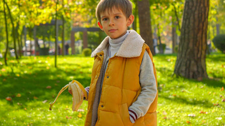 Portrait of smiling boy walking with banana at park. Child nutrition, healthy eating, snack and food outdoors.の写真素材