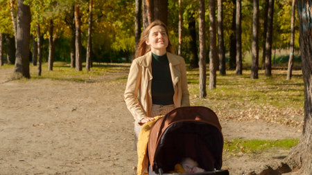Beautiful young woman walking with baby stroller at autumn park. Parenting, relaxing outdoors, beautiful mother.の写真素材