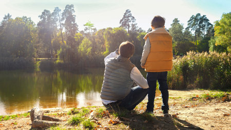 Little boy with young father standing at the lake and looking on the water. Family outdoors, happy parenting and childhood, autumn landscape, kids and parents relaxing outsideの写真素材