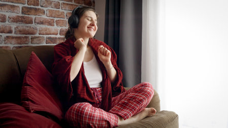 Happy cheerful woman dancing on sofa while listening music in earphones. People relaxing at home, having fun, positive emotions and joyの写真素材
