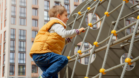 Happy smiling boy climbing up high on the rope net or spider web at outdoor playgroundの写真素材
