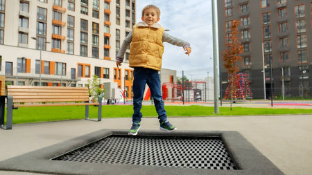 Happy smiling boy laughs and enjoys jumping on the trampoline. Active child, sports and development, kids playing outdoorsの写真素材