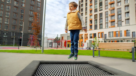 Cheerful smiling boy jumping up high on the outdoor trampoline at playground in park.の写真素材