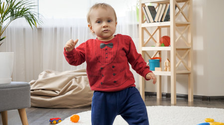 1 year old baby boy standing up and making first steps on carpet in living roomの写真素材