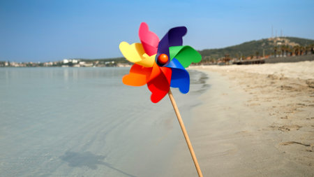 Colorful pinwheel spinning in the wind on a sandy beach, evoking the concepts of travel, summer holiday, vacation, beach tourism, and joyの写真素材