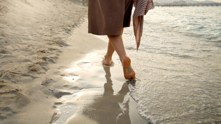 Closeup of barefoot woman walking on the wet sand and sea waves at the sandy beach on sunsetの写真素材