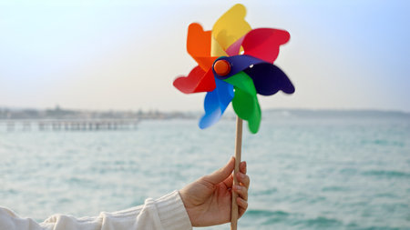 Young woman playing with a colorful spinning pinwheel on the sandy sea beach. Summer holiday, travel, and positive emotionsの写真素材