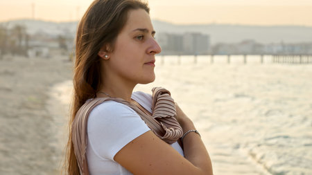Portrait of elegant woman with long hair standing on sea beach at windy day and looking at ocean.の写真素材