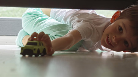 Little boy in pajamas looking under the bed and searching for lost toy car.の写真素材