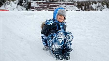 Joy of a child as he sleds down a snowy hill on his feet, with the footage slowed down to accentuate every moment of the thrilling rideの写真素材
