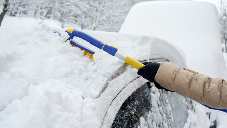 Close-up of a woman using a snow brush to remove snow from her car's windshield after a heavy...