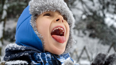 Happy cheerful boy catching falling snowflakes with his tongue. Fun and joy on winter holidays, kids playing outdoors, activity in snowfallの写真素材