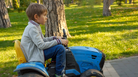 Happy boy riding on toy tractor at park. Kids playing in park, farming, driving transport.の写真素材