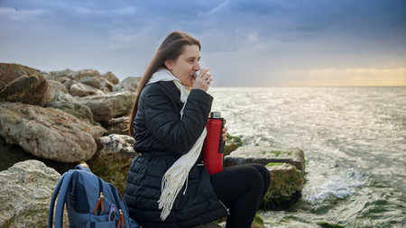 Young woman feeling cold sitting on the cliffs and looking at the cold northern sea. Concept of...