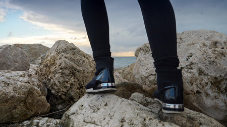 Young woman with a backpack hiking and climbing on the cliffs at the sea coast at sunset. A concept...