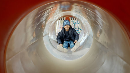 Little boy sliding down the tube slide on public playground. Happy kids, fun outdoors, leisure in parkの写真素材
