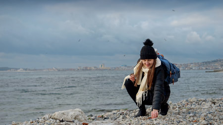 Young smiling woman with backpack walking and on the beach and searching for beautiful sea shells....