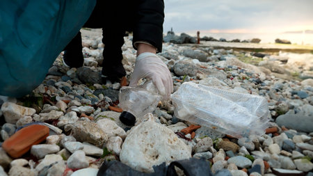Young woman volunteer walking on the sea beach and collecting garbage and wastes in plastic bag....