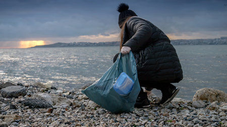 Young woman cleaning beach from garbage and trash and collecting all wastes in plastic bag.