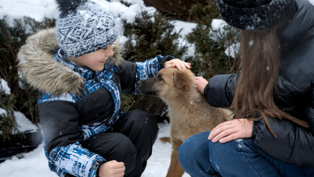 Happy smiling boy looking at cute puppy dog and comforting it with hand at house backyard on a snowy...