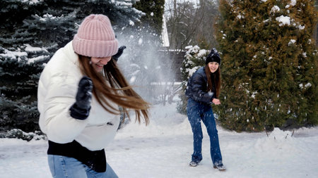 Two happy laughing teenage girls playing snowballs in backyard on snowy winter day. People playing...