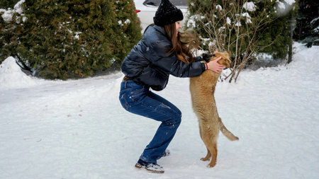 Happy teenage girl playing with her puppy in snow at house backyard. Kids with animals, games with petsの写真素材