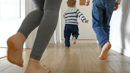 Closeup of mother and two boys running on the wooden floor at home. Concept of family love, joy, and fun in a household.の写真素材