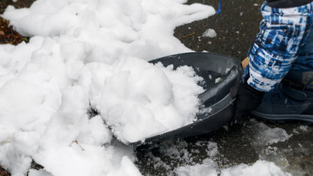 Little boy is shown removing snow from the backyard or walkway with a shovel after a snowstorm or blizzardの写真素材