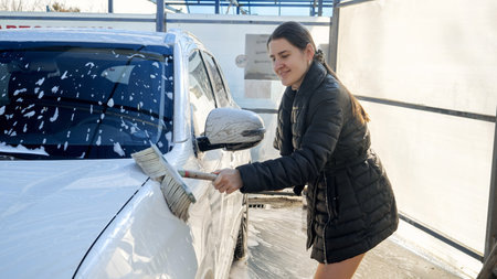Beautiful smiling woman taking care of her car and washing automobile by herself at self service car wash.の写真素材