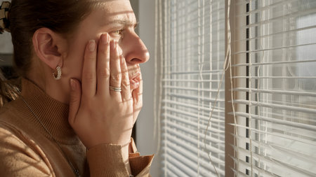 Young woman being witness of something scary or criminal while looking through window blinds.の写真素材