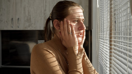 Young scared woman got shocked and terrified after looking outdoors through window blindsの写真素材