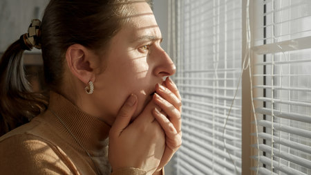 Stressed and afraid woman closing her mouth while being witness of crime or catastrophy through window.の写真素材