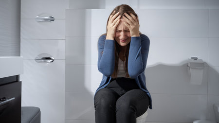 Young upset woman sitting on toilet alone and crying.の写真素材