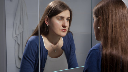 Sad young brunette woman looking at herself in mirror. Concept of depression, stress, mental illness and problems, loneliness and frustrationの写真素材