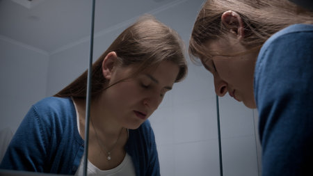 Upset and stressed woman leaning on mirror with head. Concept of depression, suicide, stress, mental illness, loneliness and frustrationの写真素材