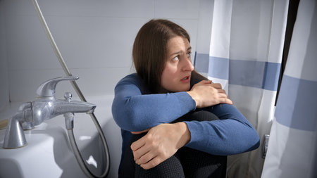 Afraid stressed woman siting in bath and looking at shadow of criminal entering bathroom. Concept of domestic violence victim, stress, danger at home, fear.の写真素材