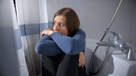 Scared woman being victim of domestic violence and abuse hiding in bath.の写真素材