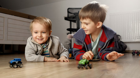 Two little brothers playing together with toy cars on floor. Children playing alone, development and education, games at homeの写真素材