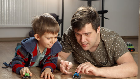 Little boy playing with his father with toy cars on floor. Children playing alone, development and education, games at homeの写真素材