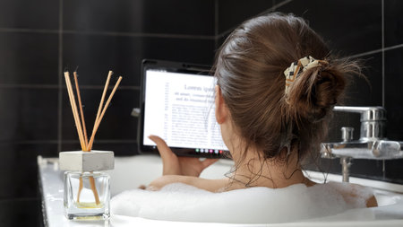 A Woman Takes a Bath and Uses Her Tablet Computer for Work or Play. Working at home, modern technology, remote jobの写真素材