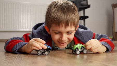 Portrait of cute smiling boy lying on floor and playing with toy cars.の写真素材