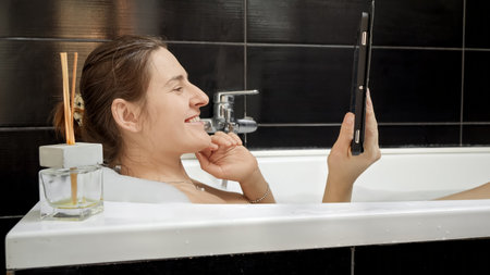Woman enjoying a bath while keeping in touch via a video call on her tablet computer. Perfect for showcasing the modern ways we stay connected while prioritizing self-care.の写真素材