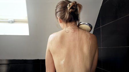 Rear view of young woman washing in bathroom with window. Importance of maintaining good hygiene and self-care routinesの写真素材
