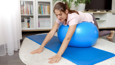 Happy smiling woman rocking and rolling on fitball during home fitness training. Concept of healthcare, sports and yoga at homeの写真素材