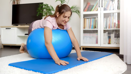 Smiling young woman lying on fitball and rolling over. Concept of healthcare, sports and yoga at homeの写真素材