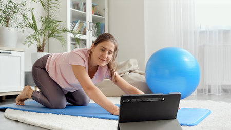 Happy smiling woman waving to her online sportrs training while watching fitness lesson on tablet computer. Concept of healthcare, sports and yoga at homeの写真素材